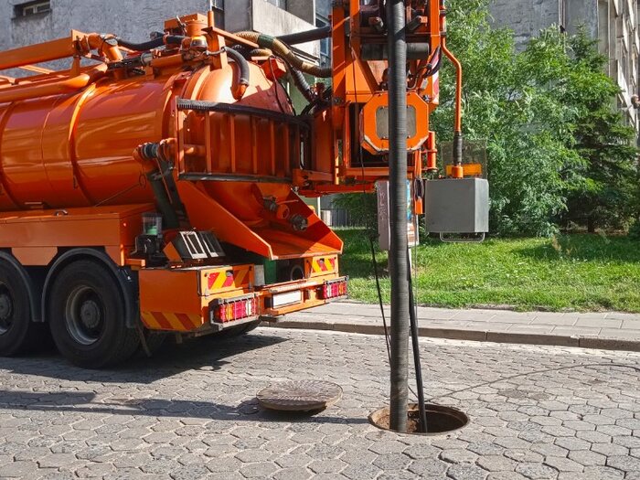 Wąż ssawny opuszczony do studzienki kanalizacyjnej przy pomarańczowym wozie ZIĘBUD we Wrocławiu