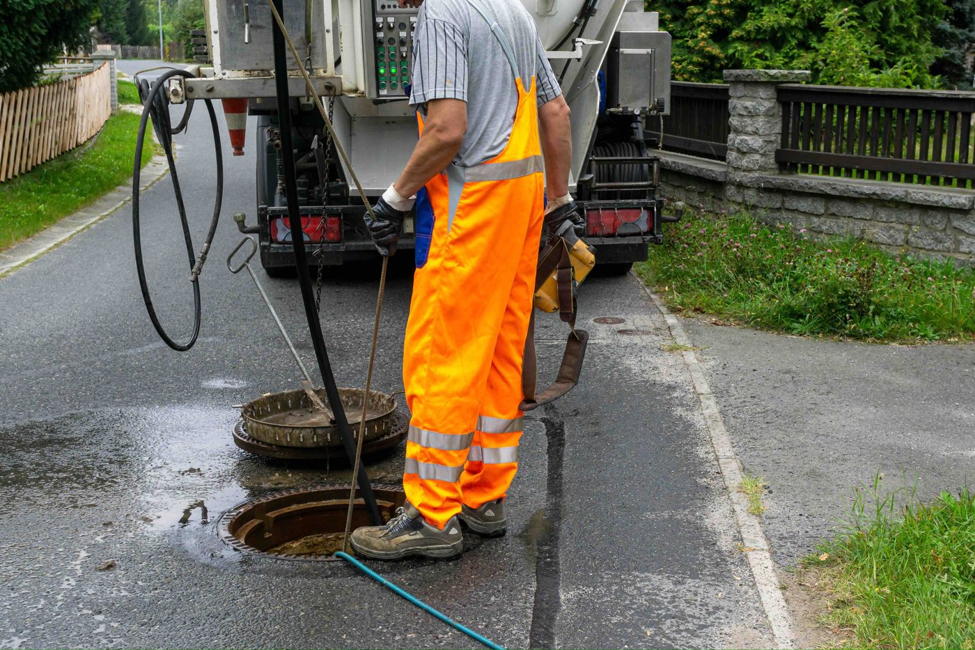 Pracownik z wężem przy otwartej studzience kanalizacyjnej