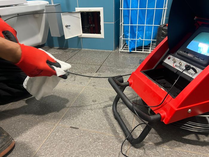 Pracownik prowadzi diagnostykę instalacji kamerą inspekcyjną Rothenberger w łazience, przy otwartej kratce rewizyjnej w ścianie