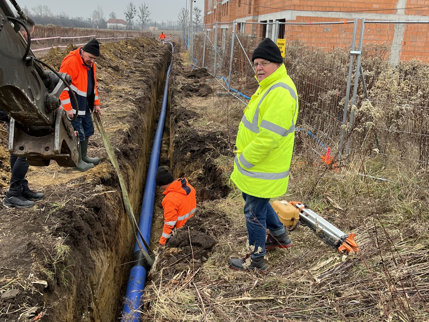 Układanie niebieskiej rury PE przyłącza wodociągowego w wykopie liniowym, pracownicy ZIĘBUD w kamizelkach ostrzegawczych